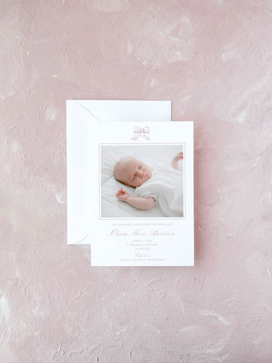 Elegant birth announcement card featuring a delicate pink bow and a soft photo of a sleeping newborn on a textured light pink background.