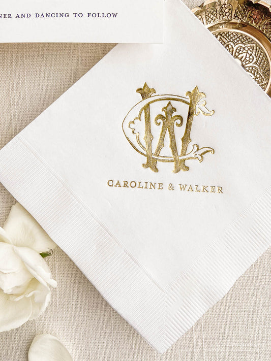 White cocktail napkin with gold embossed monogram and elegant personalized wedding details on textured fabric background