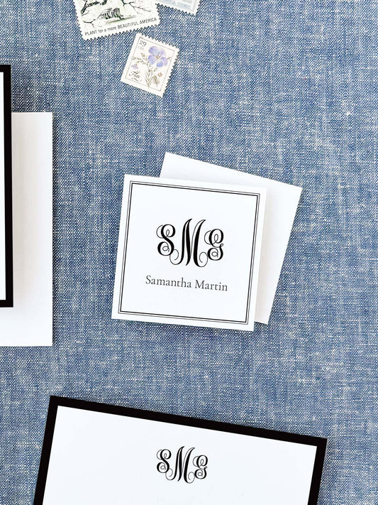 Personalized black and white calling card featuring elegant monogram and classic serif name font, displayed on textured blue fabric background.