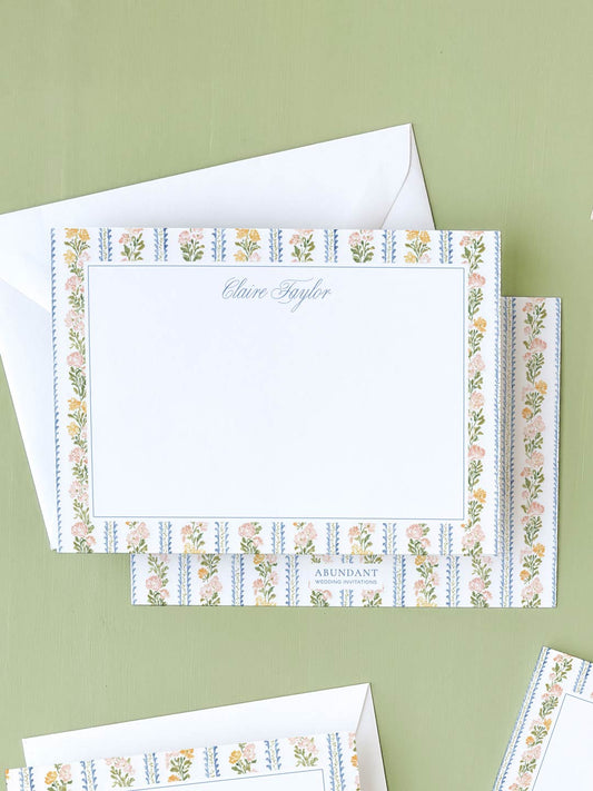Flat notecard featuring delicate botanical stripe border with floral accents on white background and matching envelope.