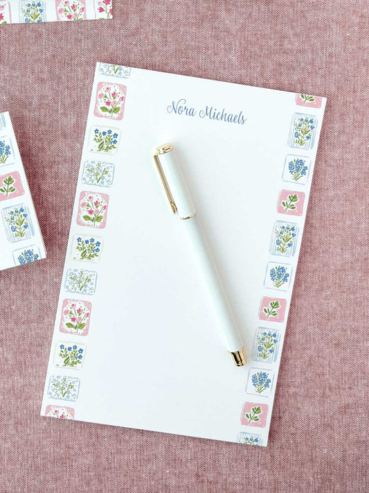 Personalized floral tile notepad with delicate pink and blue flower illustrations and a white pen on fabric background