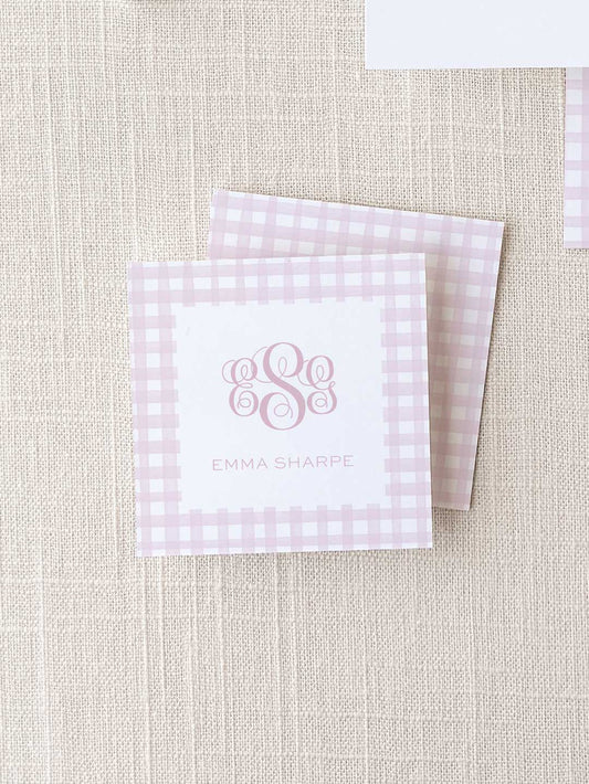 Pink gingham patterned calling cards with elegant monogram initials and personalized name text on a textured neutral background