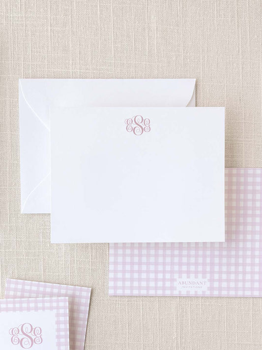 Elegant white notecard with a delicate pink monogram above, paired with matching pink gingham patterned stationery and envelope for personalized correspondence.