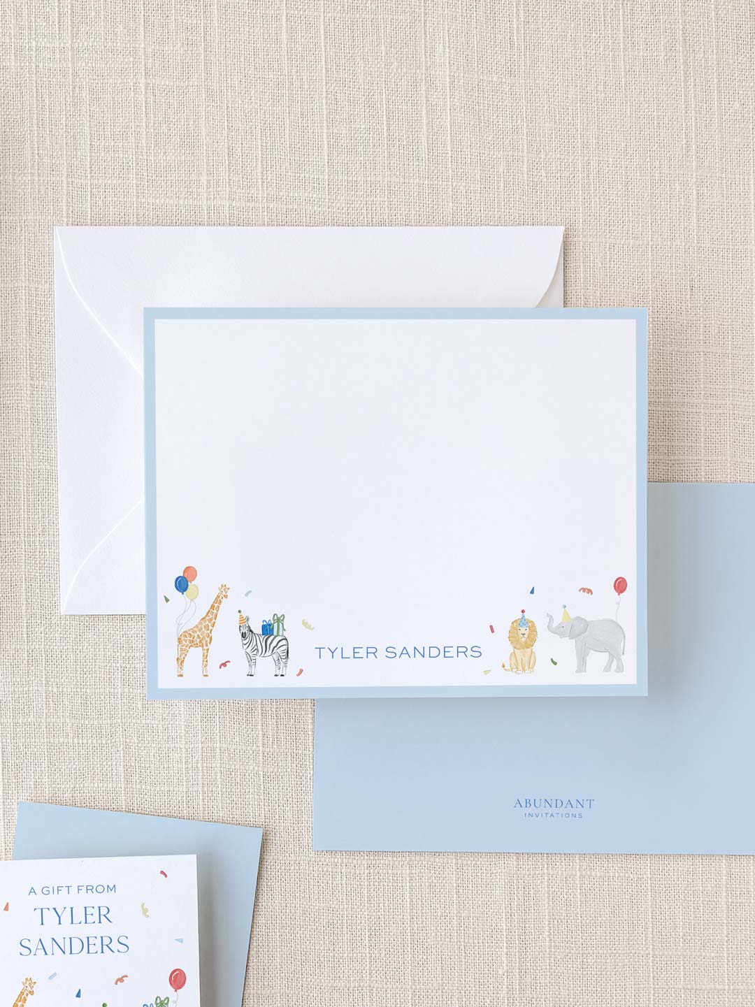 Flat notecard with a light blue border featuring colorful illustrated animals including a giraffe, zebra, lion, and rhinoceros with personalized name text.