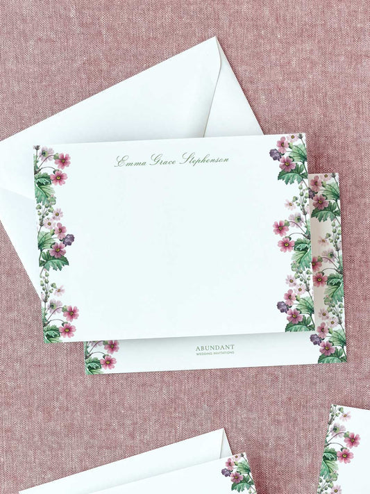 Personalized flat notecard with delicate primrose floral borders and elegant script on textured fabric background.