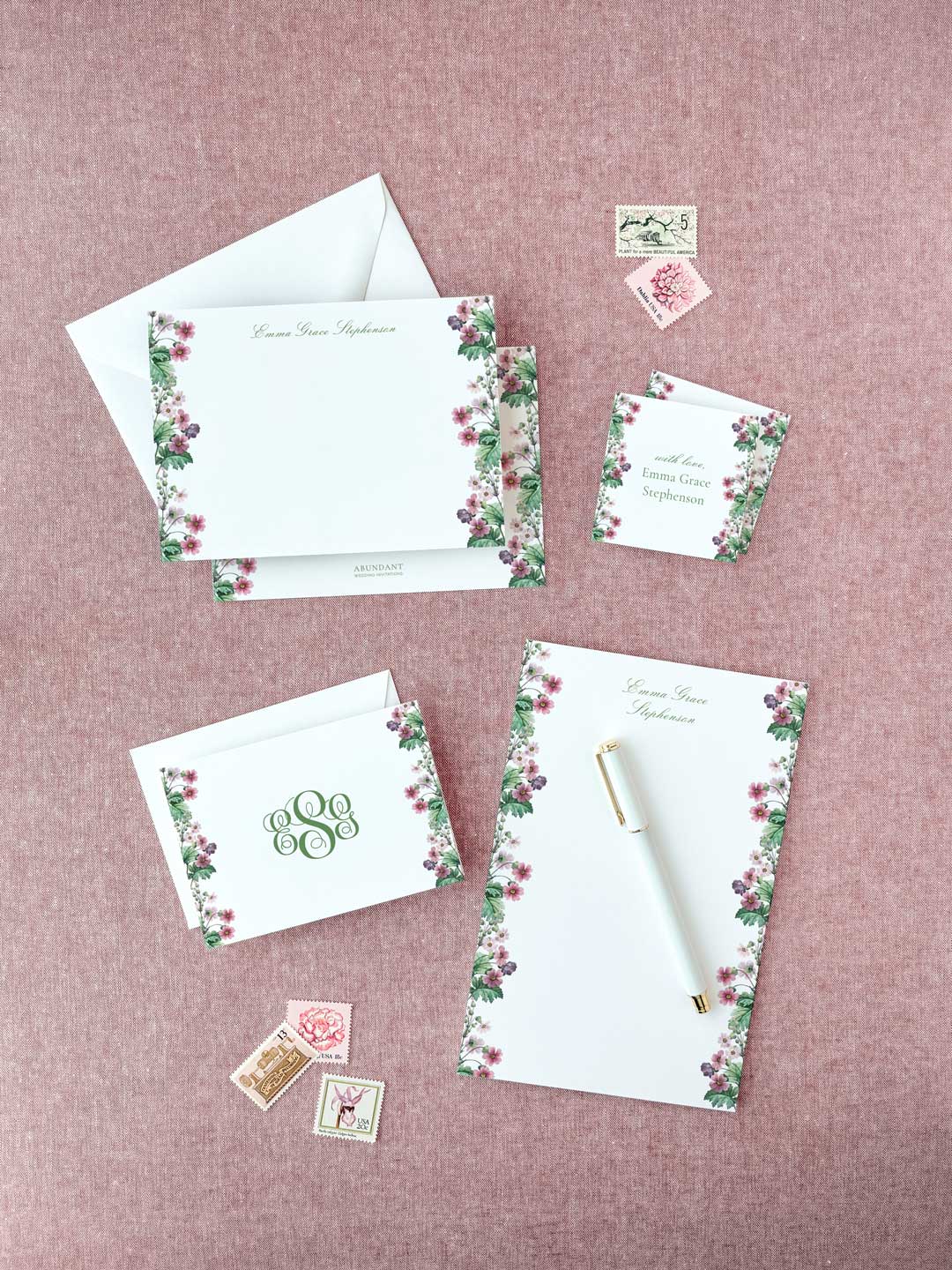 Elegant stationery set with floral borders featuring personalized notepad, envelopes, and vintage-style stamps on pink background