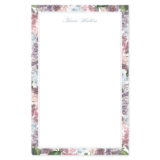 Notepad with a blue, pink, and purple hydrangea floral border design with a personalized script name on a white background