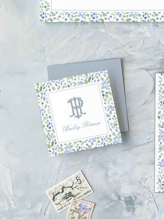 Square calling card with watercolor floral border and elegant monogram on textured gray surface