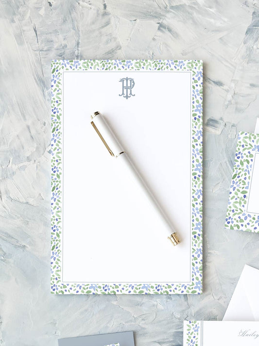 Elegant notepad with blue and green watercolor floral border and a white pen on textured surface