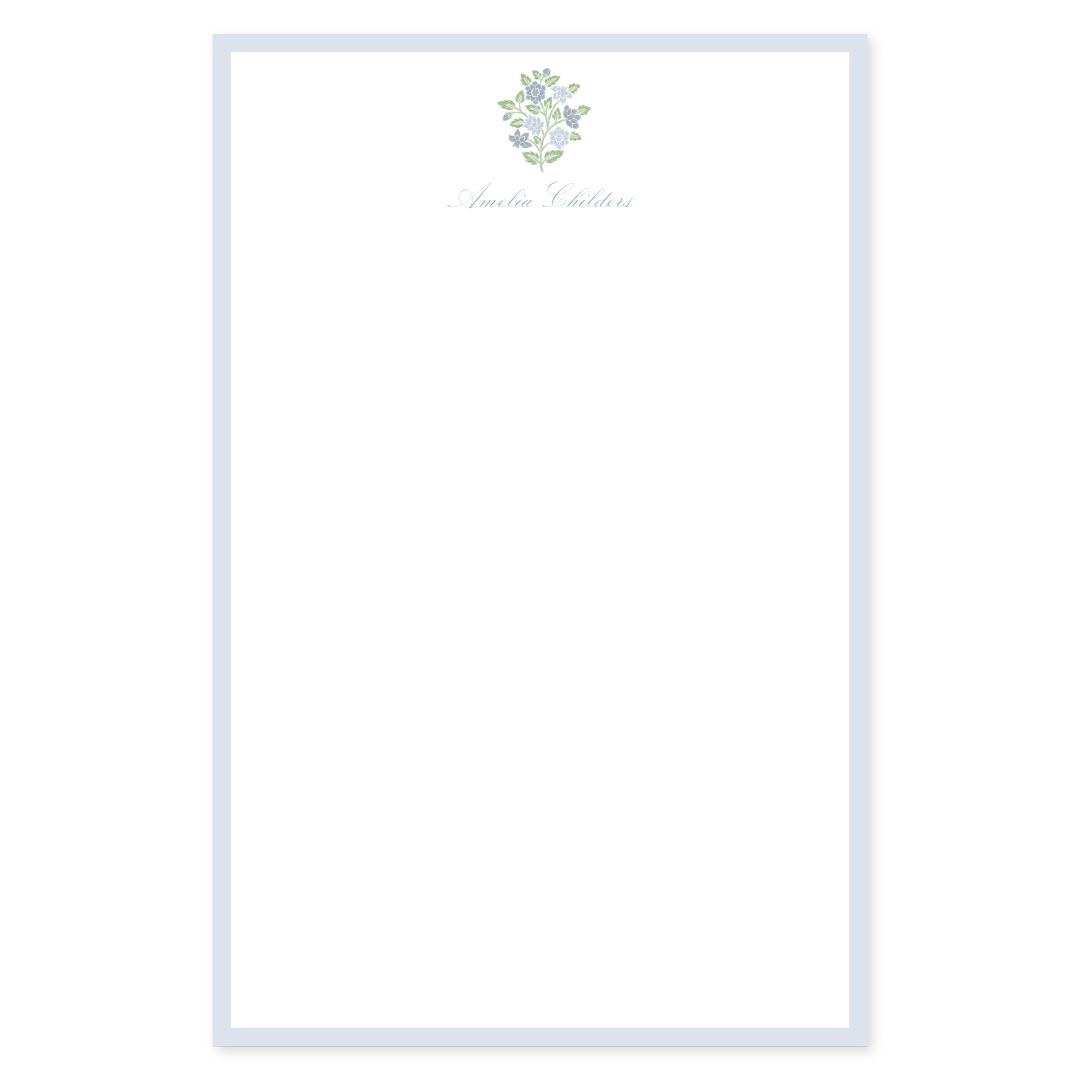 Personalized notepad with a light blue border, blue and green block floral element, and custom script name on white paper