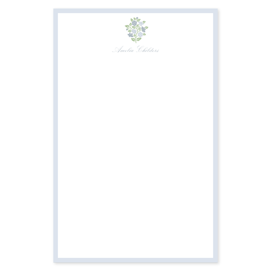 Personalized notepad with a light blue border, blue and green block floral element, and custom script name on white paper