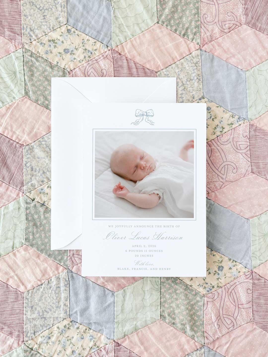 Birth announcement card with a soft blue bow illustration, featuring a photo of a sleeping newborn on a pastel patchwork quilt background.
