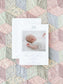Birth announcement card with a soft blue bow illustration, featuring a photo of a sleeping newborn on a pastel patchwork quilt background.