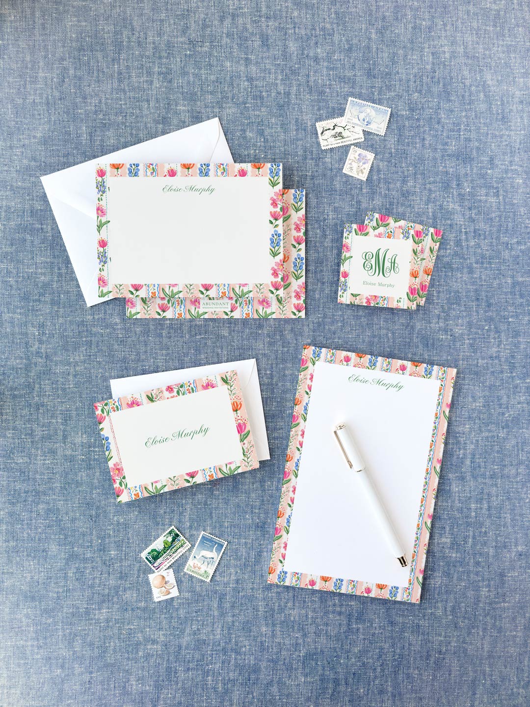 Floral bordered stationery set with personalized name on cards and notepad, styled on blue fabric background