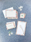 Floral bordered stationery set with personalized name on cards and notepad, styled on blue fabric background