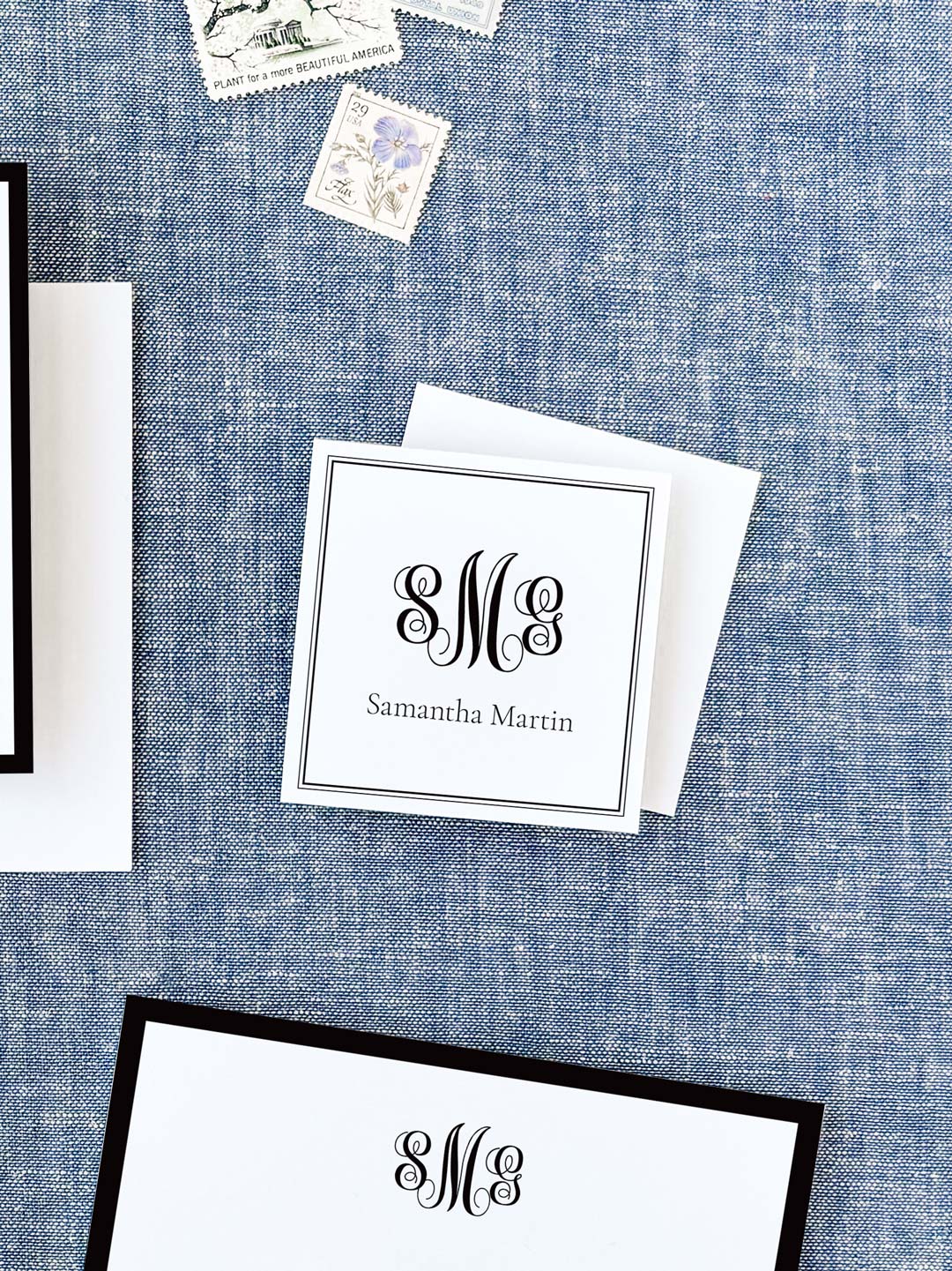 Personalized black and white calling card featuring elegant monogram and classic serif name font, displayed on textured blue fabric background.