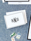 Elegant folded notecard with black monogram initials and a thin double-line border resting on a textured blue fabric background with vintage postage stamps nearby.