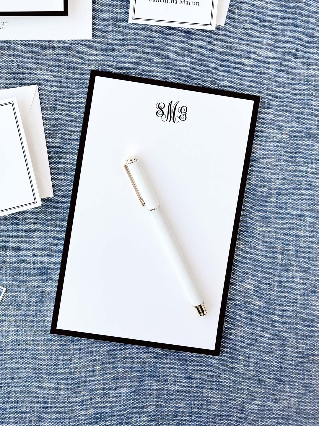 Personalized notepad featuring a classic black border and elegant monogram, displayed with a white pen on textured fabric background.