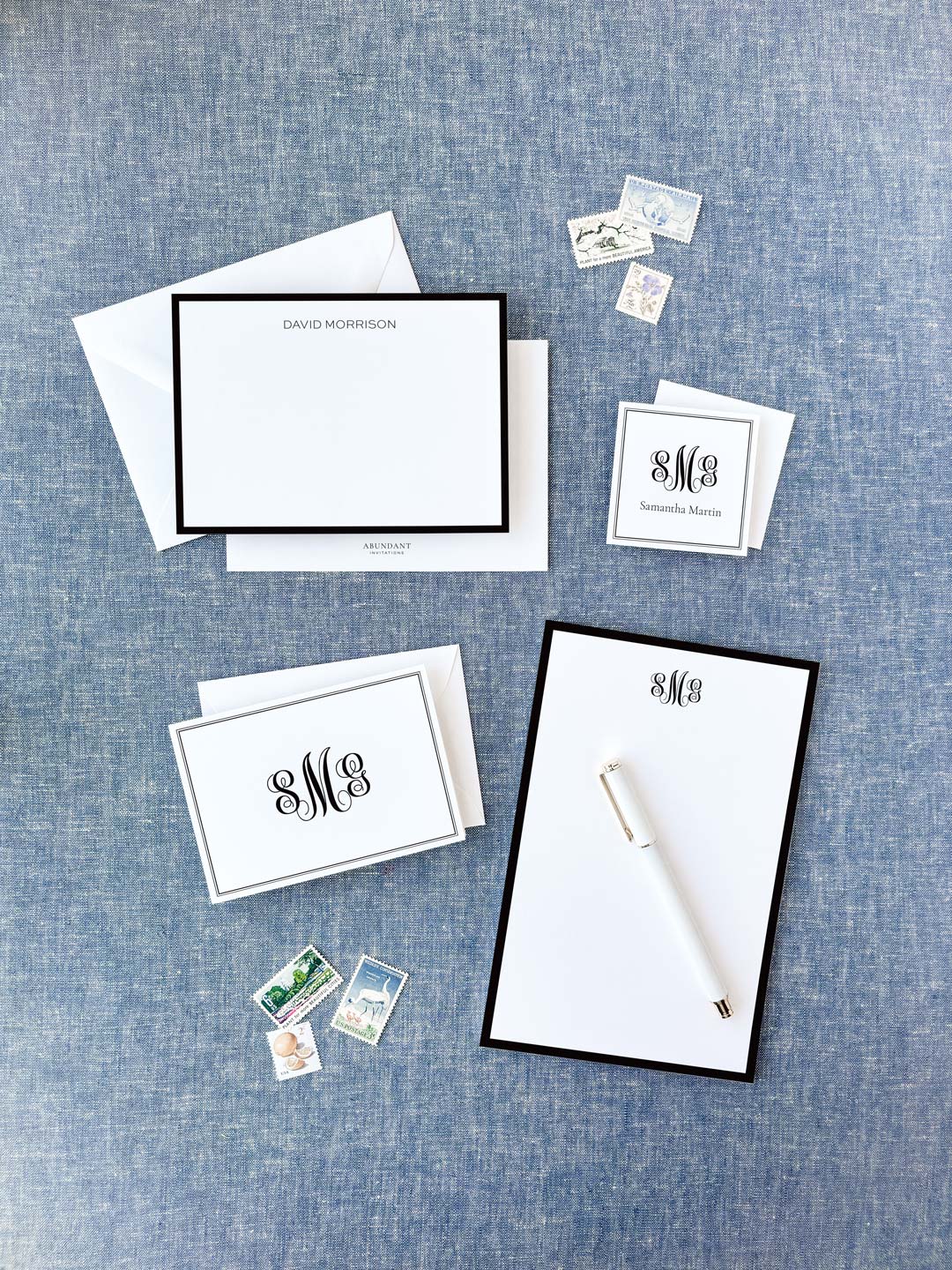 Elegant personalized stationery set featuring classic black bordered cards and notepad with monogram initials on a textured blue background.