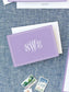 Folded lavender notecard with elegant white monogram on textured blue background, paired with white envelope and vintage postage stamps.