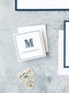 Square personalized calling card with a navy monogram letter and name on white textured background, accompanied by vintage stamps.