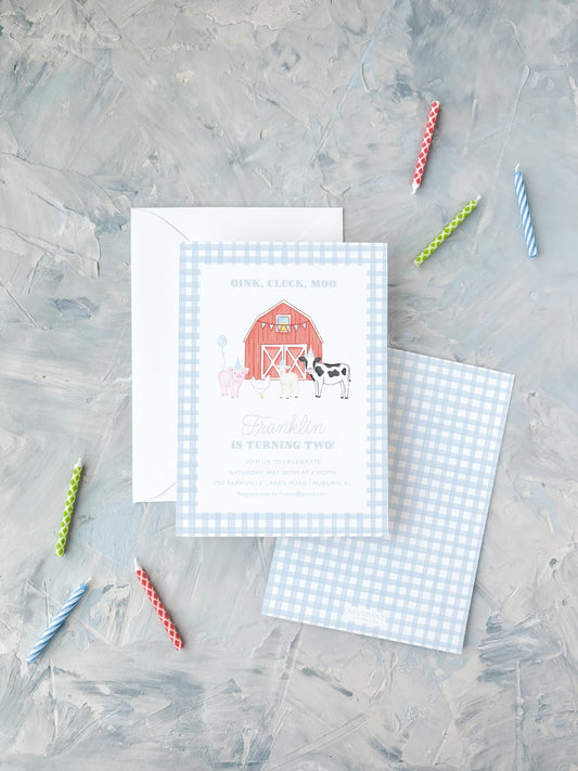 Blue checkered birthday invitation with farm animals and red barn, surrounded by colorful candles on gray surface