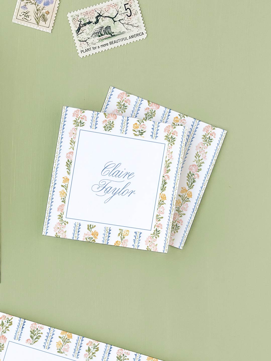 Stack of floral stripe calling cards featuring elegant script and delicate botanical border designs on a soft green background