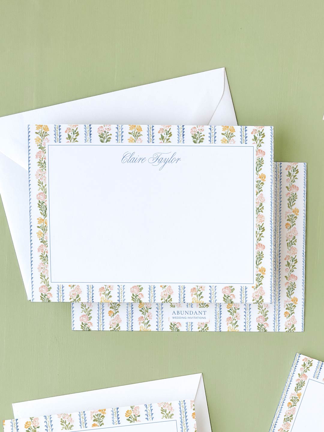 Flat notecard featuring delicate botanical stripe border with floral accents on white background and matching envelope.
