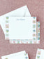 Personalized flat notecard with delicate floral tile border and matching envelope on a textured surface.