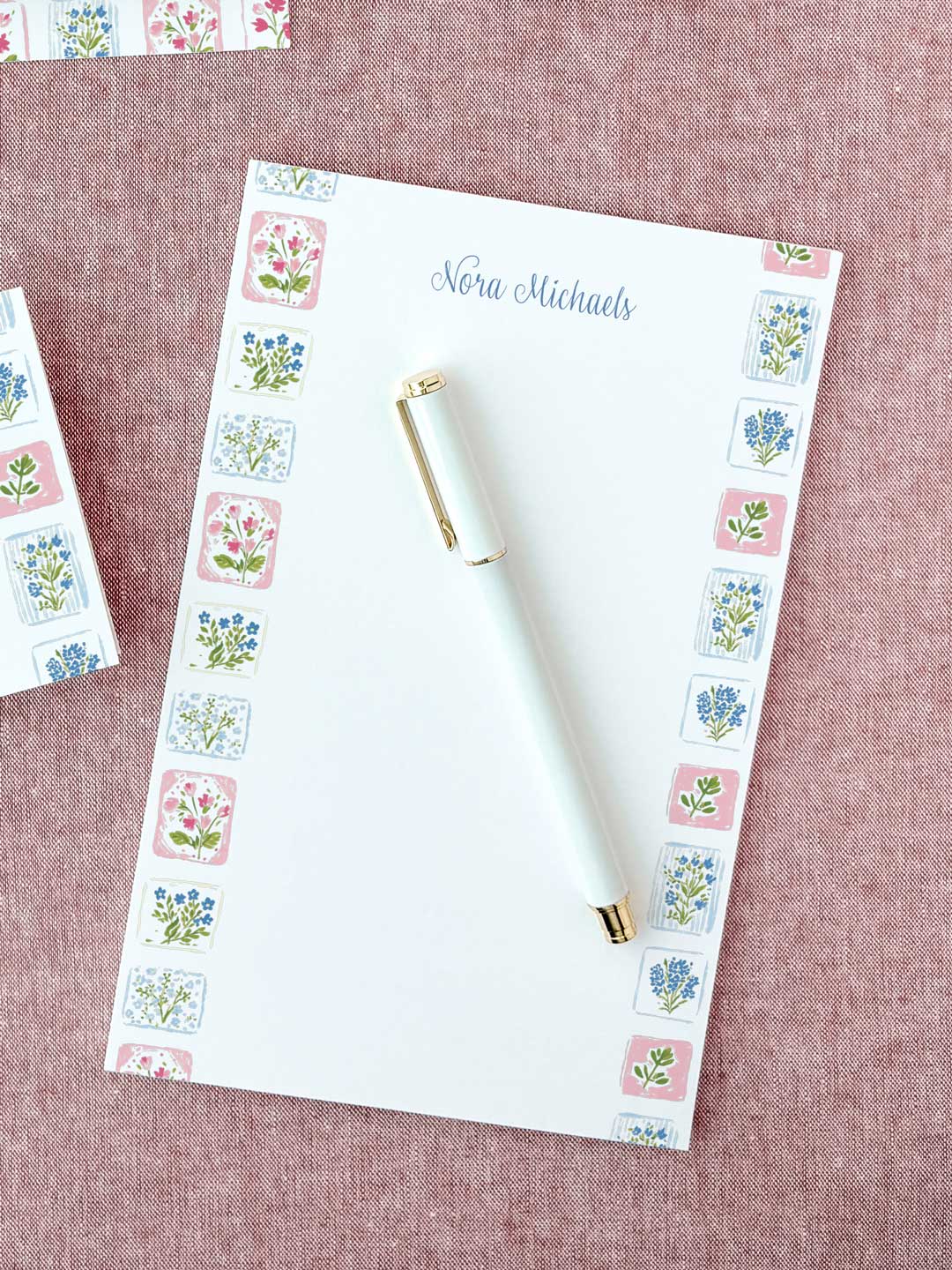 Personalized floral tile notepad with delicate pink and blue flower illustrations and a white pen on fabric background