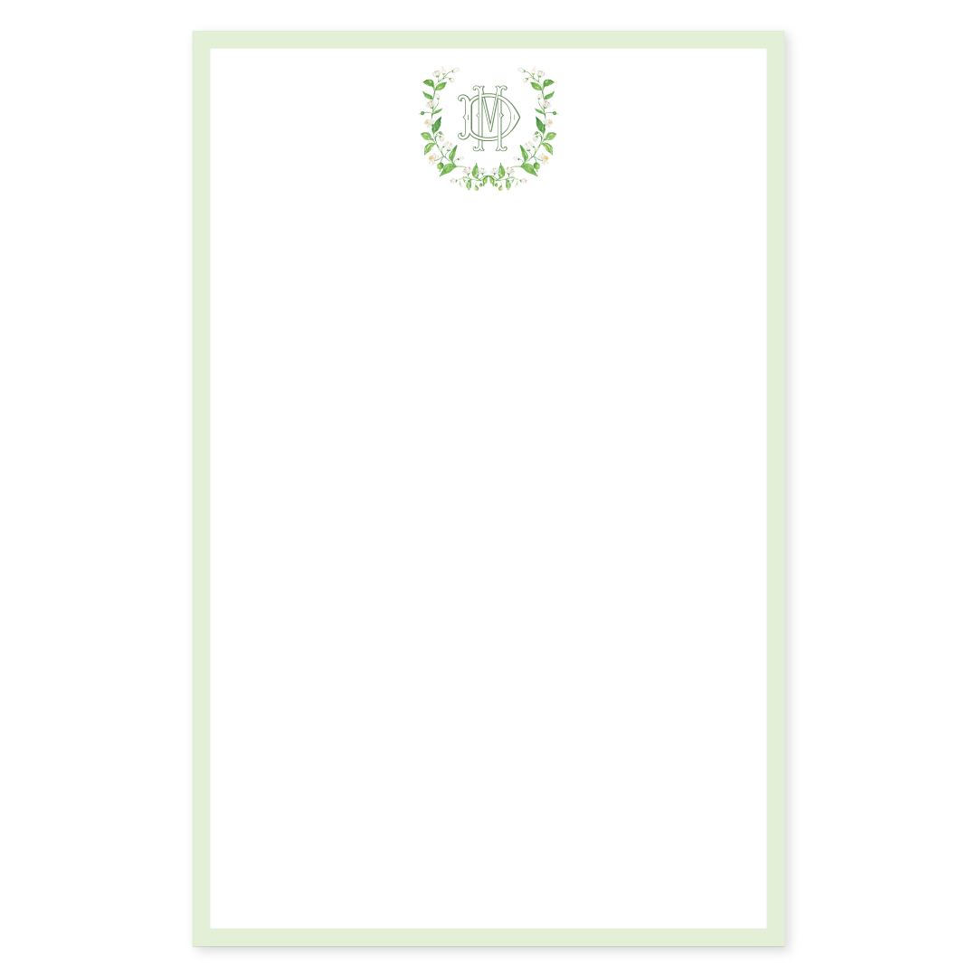 Personalized notepad with a decorative white flower wreath surrounding an interlocking monogram on a white background with a green border