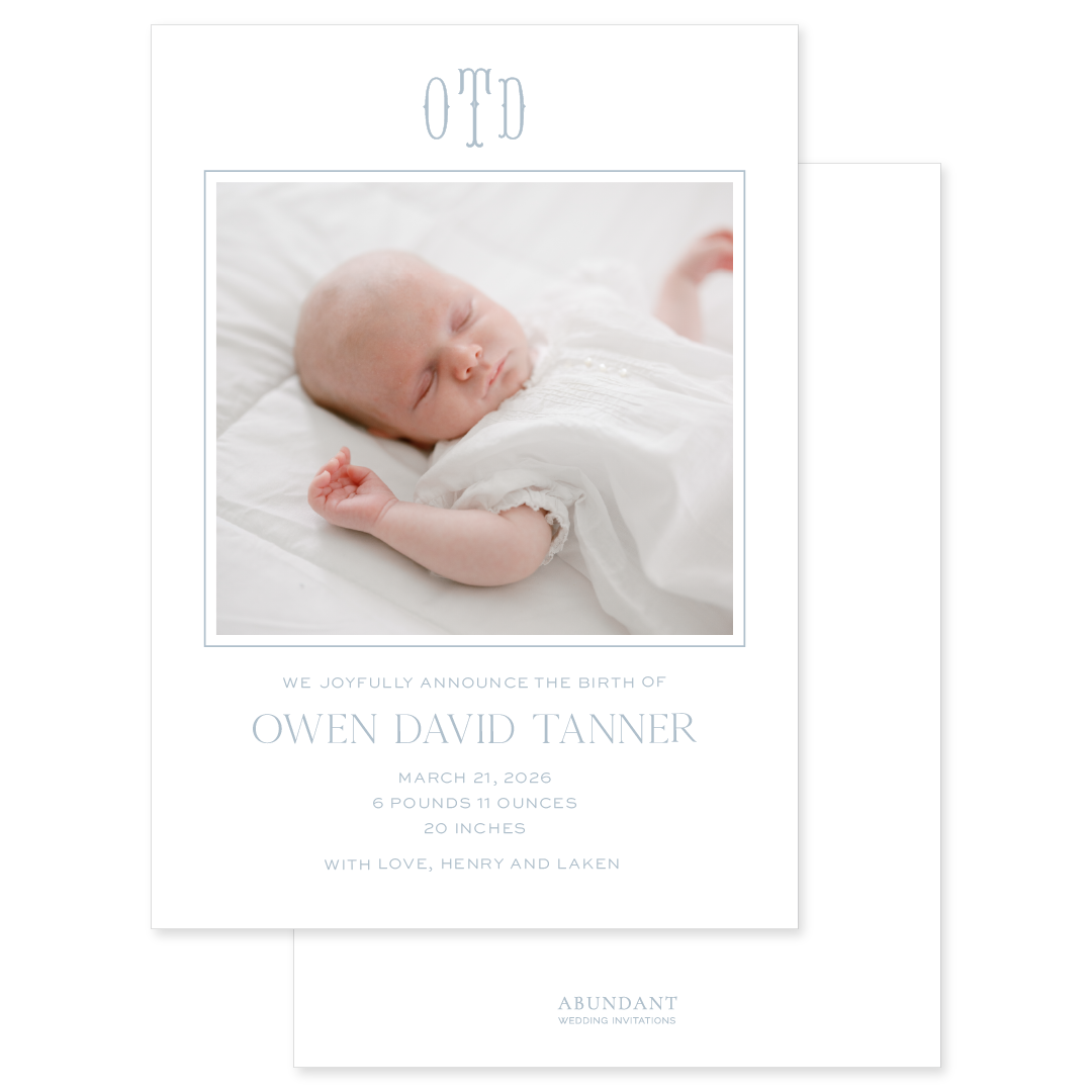 Newborn baby announcement card with a photo of a sleeping baby and baby blue text and monogram details.