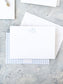 White flat notecard with light blue monogram lettering, paired with a matching blue gingham patterned envelope on a textured stone surface.