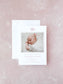 Elegant pink monogrammed birth announcement card featuring a photo of a sleeping newborn, presented with a matching white envelope on a soft pink background.