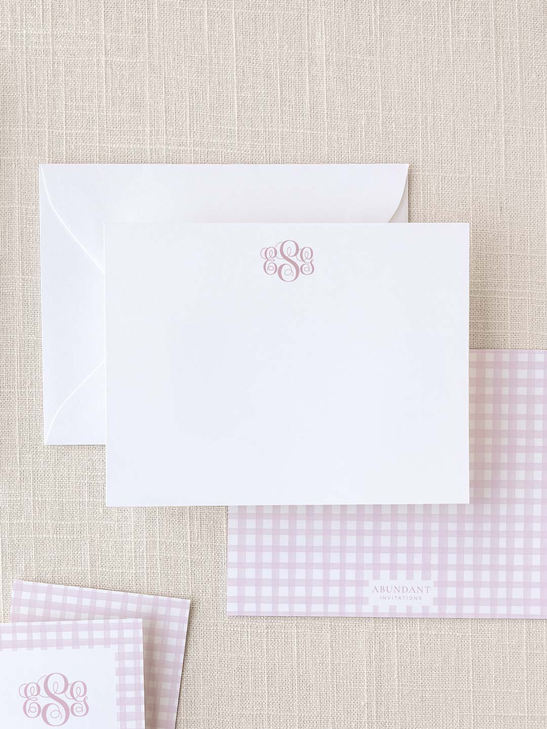 Elegant white notecard with a delicate pink monogram above, paired with matching pink gingham patterned stationery and envelope for personalized correspondence.