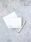 Personalized flat notecard with playful animal illustrations and light blue border, accompanied by a white envelope and elegant pen on textured background.