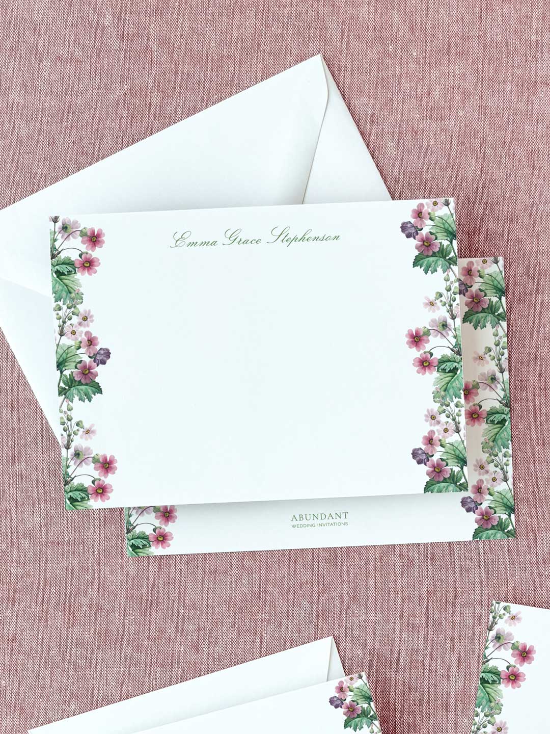 Personalized flat notecard with delicate primrose floral borders and elegant script on textured fabric background.