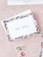 Folded notecard with delicate watercolor floral border on soft pink background, personalized elegant calligraphy name center.
