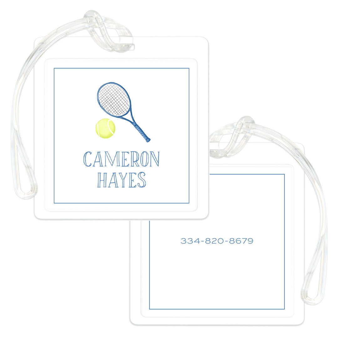 Two square blue and white bag tags with clear straps, one displaying a tennis racket and ball above a personalized name, the other showing a phone number.