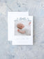 Birth announcement card featuring a sleeping baby photo bordered by a delicate blue watercolor bow, displayed with a white envelope on a textured pale background.