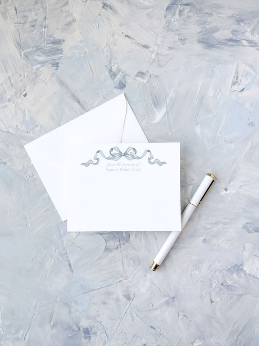 Elegant flat notecard featuring a delicate blue watercolor bow design, paired with a matching envelope and white pen on a textured surface.