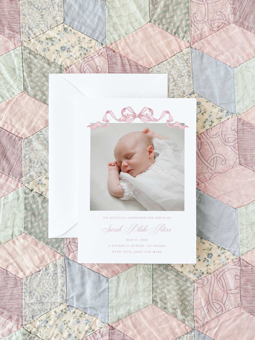 Birth announcement card featuring a sleeping baby dressed in white, decorated with a delicate pink watercolor bow on a soft pastel patchwork quilt background.