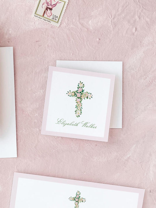 Square card with a floral watercolor cross and elegant cursive name on a soft pink textured background