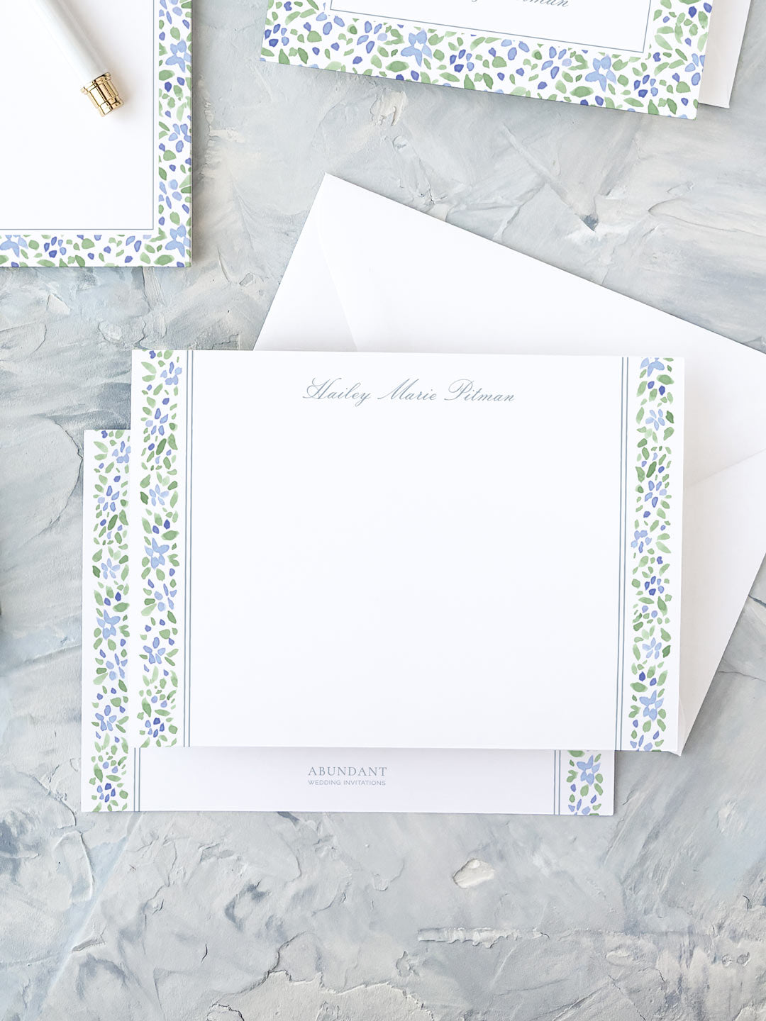 Elegant personalized flat notecard with watercolor floral stripe border in soft blue and green hues on white background.