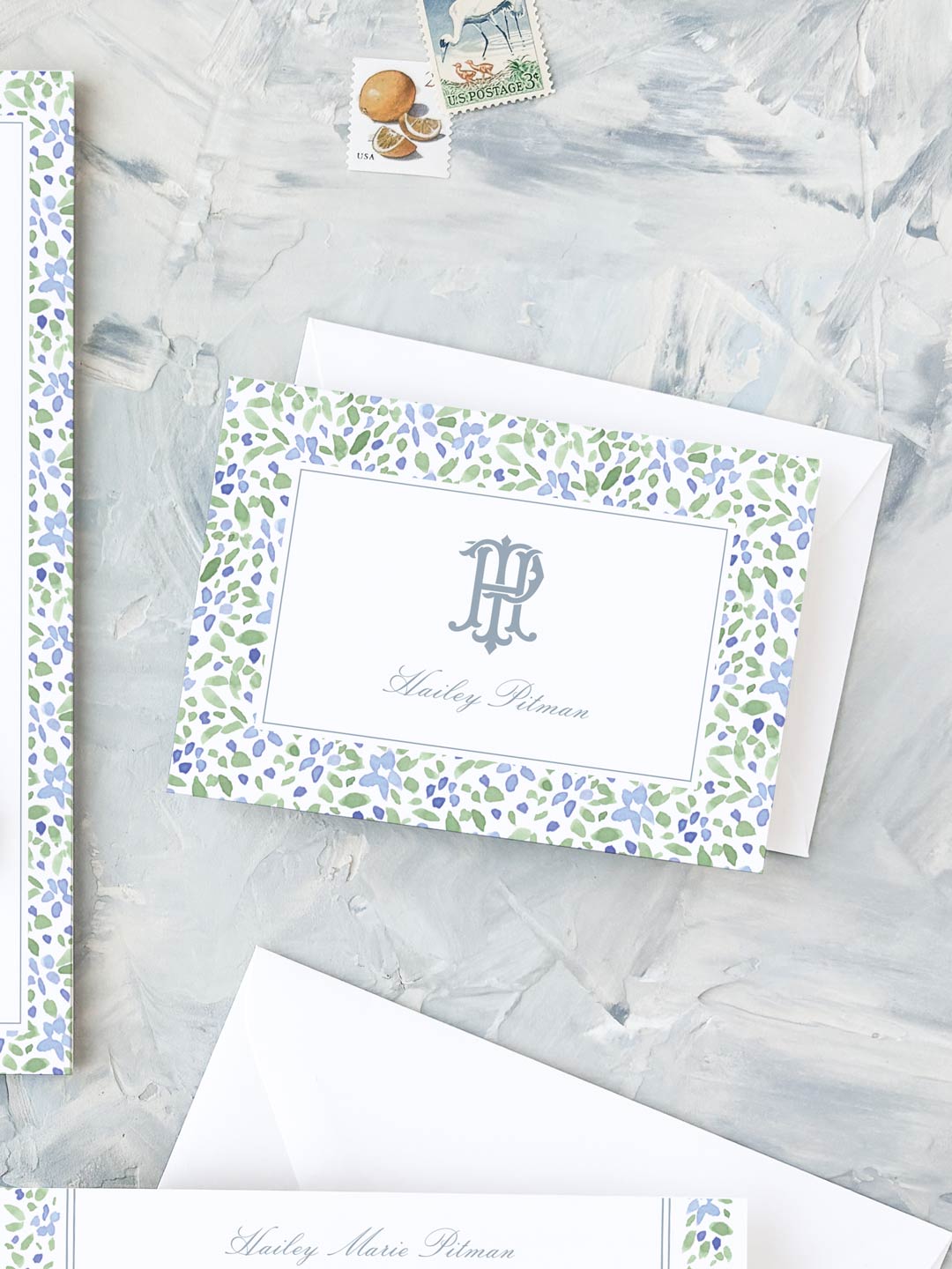 Folded notecard with watercolor floral border and elegant personalized monogram on textured background