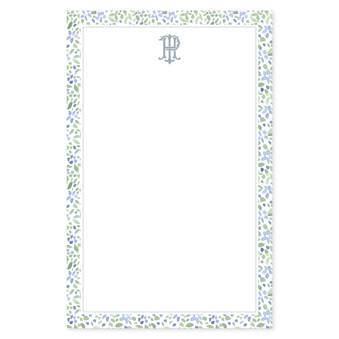 Notepad with a loose watercolor floral border in blue and green with an interlocking monogram on a white background
