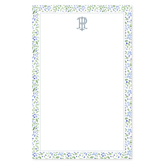 Notepad with a loose watercolor floral border in blue and green with an interlocking monogram on a white background
