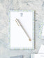 Elegant notepad with blue and green watercolor floral border and a white pen on textured surface